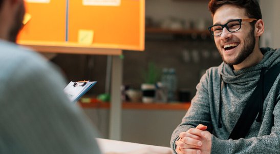 2 homens sentados de frente em uma mesa conversando