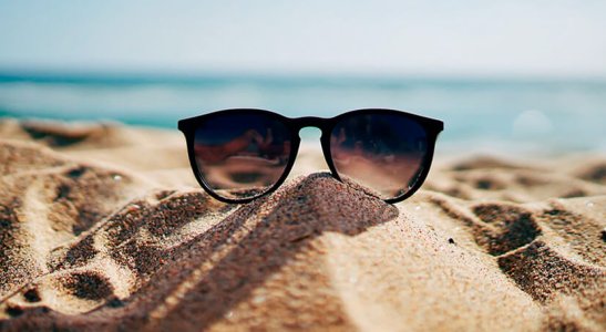 óculos de sol sobre a areia da praia com o mar ao fundo