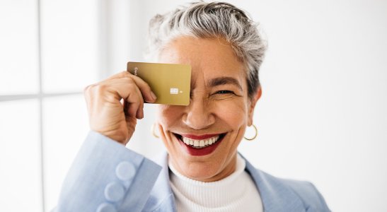 Imagem de uma mulher de meia idade com cabelos curtos e grisalhos, segurando um cartão de crédito à frente do rosto, representando a avaliação de crédito