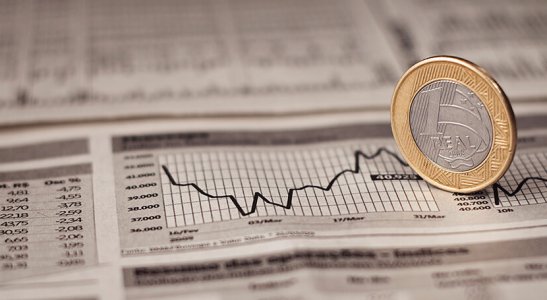 jornal com gráfico estatístico e uma moeda de R$1 de pé sobre ele