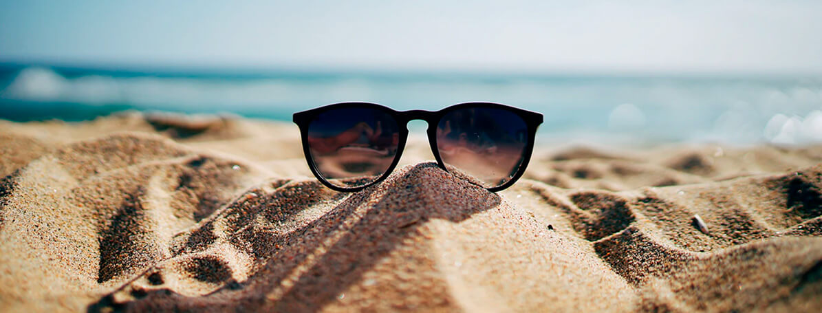 óculos de sol sobre a areia da praia com o mar ao fundo