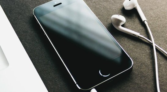 celular ao lado de notebook e fones de ouvido em uma mesa